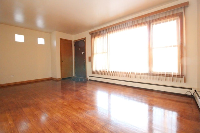 spare room featuring baseboard heating and hardwood / wood-style flooring