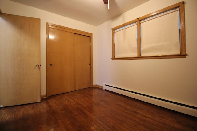 unfurnished bedroom with a closet, a baseboard heating unit, ceiling fan, and dark hardwood / wood-style floors