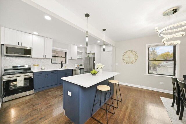 kitchen featuring stainless steel appliances, white cabinetry, blue cabinets, and pendant lighting