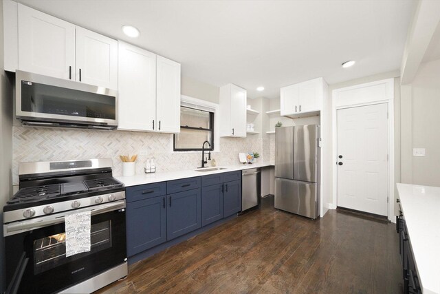 kitchen featuring appliances with stainless steel finishes, blue cabinetry, dark wood-type flooring, sink, and white cabinetry