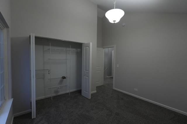 unfurnished bedroom with high vaulted ceiling, dark colored carpet, and a closet