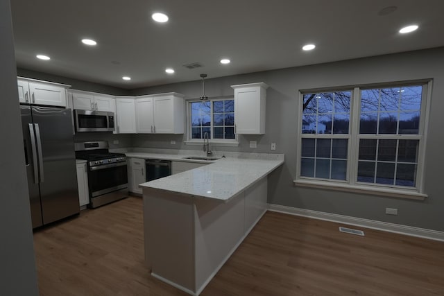 kitchen with appliances with stainless steel finishes, white cabinets, sink, and kitchen peninsula