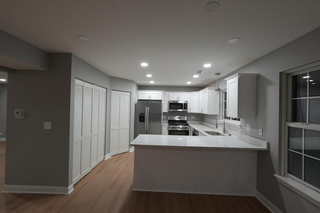 kitchen featuring kitchen peninsula, decorative light fixtures, stainless steel appliances, white cabinetry, and sink