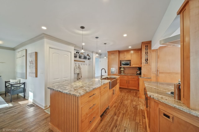 kitchen with a spacious island, sink, light stone counters, decorative light fixtures, and light hardwood / wood-style flooring