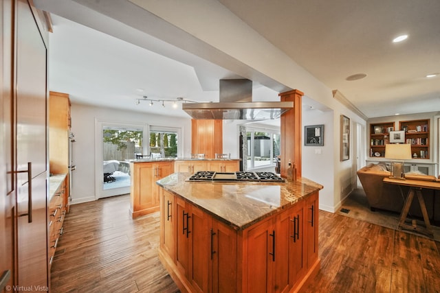 kitchen featuring stainless steel gas cooktop, island range hood, a kitchen island, light stone countertops, and hardwood / wood-style floors