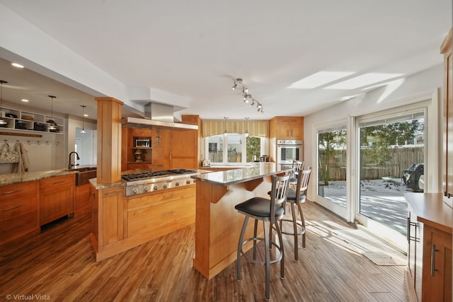 kitchen with a breakfast bar area, hardwood / wood-style floors, stainless steel appliances, a center island, and wall chimney exhaust hood