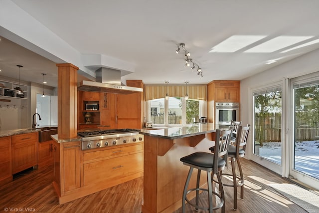 kitchen with stainless steel appliances, hanging light fixtures, a center island, and wall chimney range hood