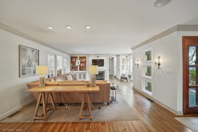 living room with crown molding, built in shelves, and light wood-type flooring