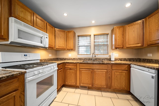 kitchen with light tile patterned floors, sink, dark stone countertops, and white appliances