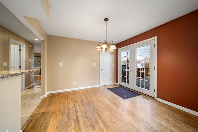 unfurnished dining area featuring light hardwood / wood-style flooring, french doors, and an inviting chandelier