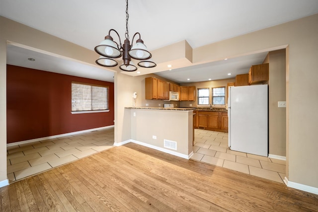 kitchen featuring white appliances, light tile patterned floors, kitchen peninsula, and an inviting chandelier