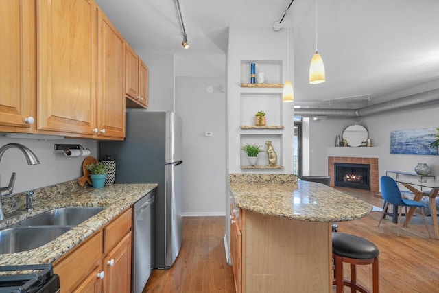 kitchen featuring light stone counters, dishwasher, a breakfast bar area, a fireplace, and sink