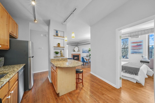 kitchen with a tiled fireplace, light hardwood / wood-style floors, track lighting, a kitchen bar, and stainless steel dishwasher