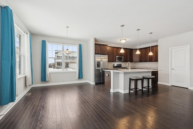 kitchen featuring stainless steel appliances, a kitchen island with sink, decorative light fixtures, dark hardwood / wood-style flooring, and a breakfast bar