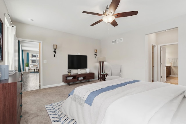 bedroom with ceiling fan, light colored carpet, and ensuite bathroom