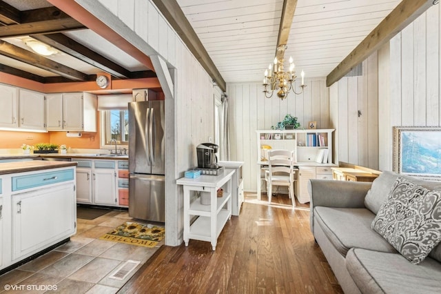 kitchen featuring a notable chandelier, beam ceiling, stainless steel refrigerator, hanging light fixtures, and white cabinets