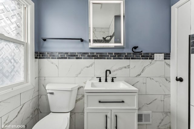 bathroom featuring toilet, vanity, and tile walls