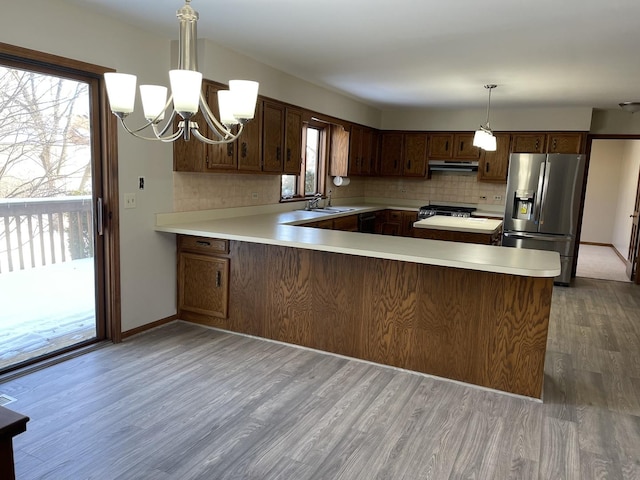 kitchen featuring pendant lighting, hardwood / wood-style flooring, an inviting chandelier, stainless steel appliances, and kitchen peninsula