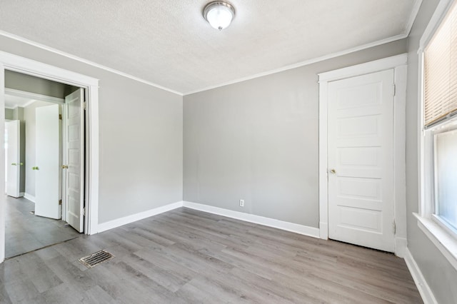 empty room with a textured ceiling, light wood-type flooring, and crown molding