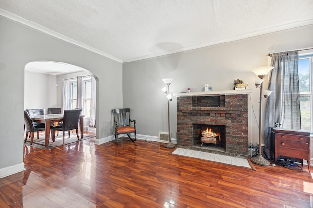 living room with a brick fireplace, a textured ceiling, ornamental molding, and wood-type flooring