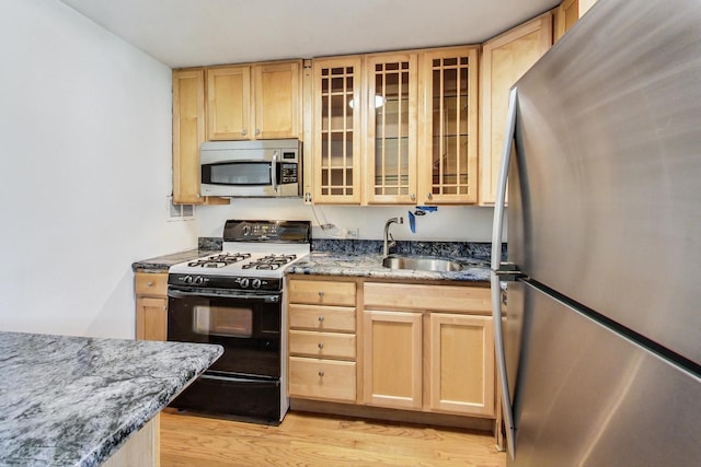 kitchen with sink, stainless steel appliances, dark stone countertops, and light brown cabinetry