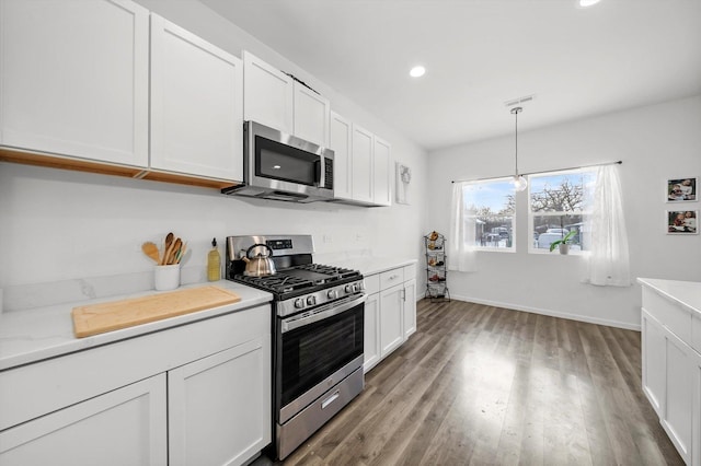 kitchen with stainless steel appliances, white cabinetry, wood-type flooring, and hanging light fixtures