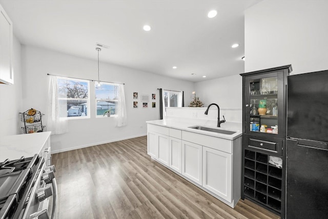 kitchen featuring white cabinetry, stainless steel range, sink, light hardwood / wood-style flooring, and decorative light fixtures