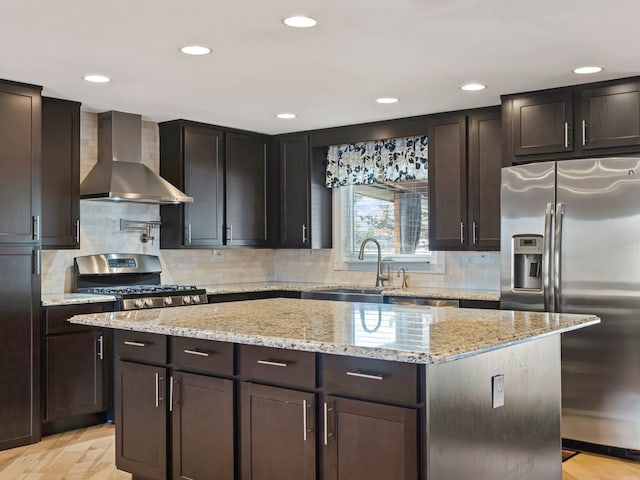 kitchen featuring stainless steel appliances, a center island, light stone countertops, wall chimney exhaust hood, and sink