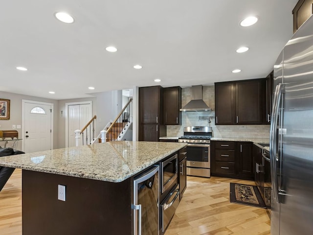 kitchen featuring light hardwood / wood-style floors, stainless steel appliances, a kitchen island, decorative backsplash, and wall chimney exhaust hood