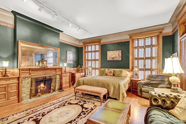 bedroom featuring a premium fireplace, rail lighting, and light hardwood / wood-style flooring