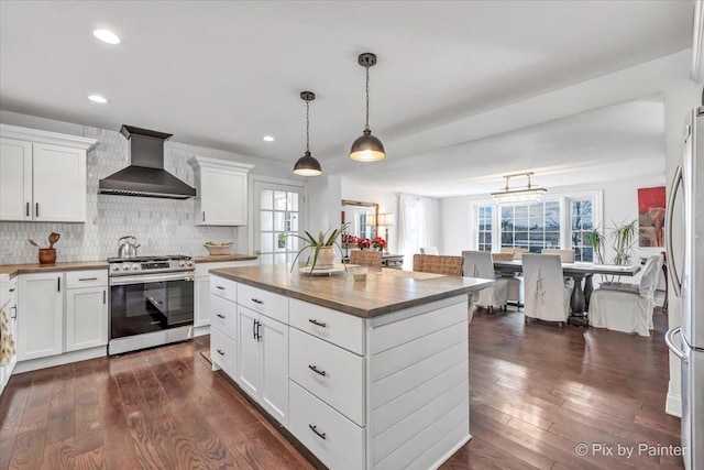 kitchen with wall chimney range hood, wood counters, stainless steel appliances, and dark wood-type flooring