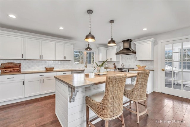 kitchen with dark wood-style floors, wall chimney exhaust hood, white cabinets, and backsplash