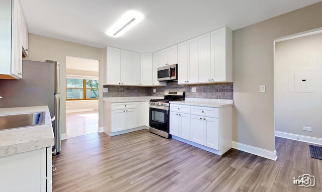 kitchen featuring stainless steel appliances, sink, white cabinets, light hardwood / wood-style floors, and backsplash