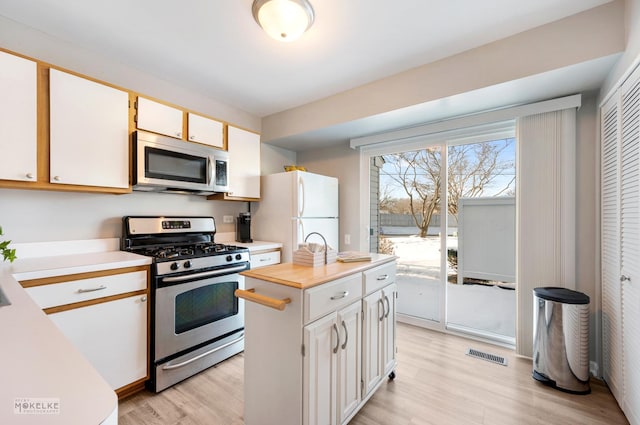 kitchen with white cabinets, stainless steel appliances, light wood-type flooring, and a center island