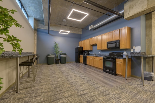 kitchen featuring kitchen peninsula, a high ceiling, a breakfast bar, black appliances, and hardwood / wood-style floors