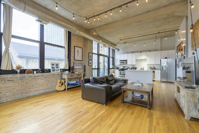 living room with a high ceiling, brick wall, floor to ceiling windows, and light hardwood / wood-style flooring