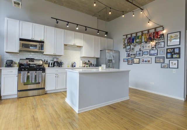 kitchen with stainless steel appliances, light hardwood / wood-style floors, backsplash, and white cabinetry