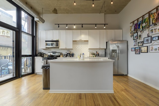 kitchen featuring stainless steel appliances, white cabinets, light hardwood / wood-style floors, decorative backsplash, and a center island with sink