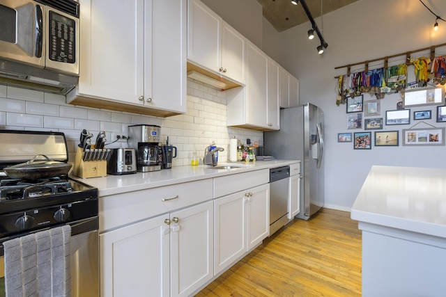 kitchen featuring rail lighting, appliances with stainless steel finishes, sink, white cabinetry, and tasteful backsplash