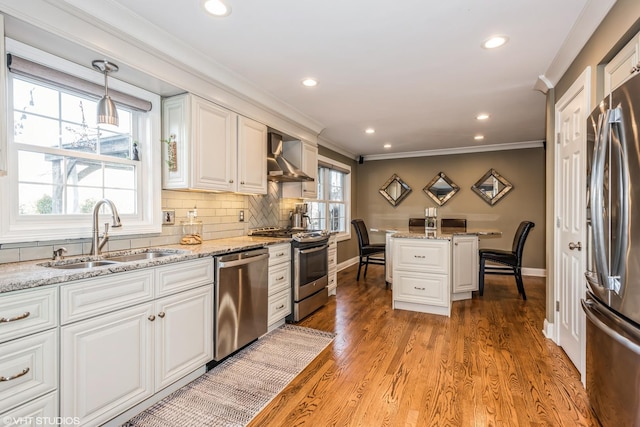 kitchen with pendant lighting, sink, wall chimney exhaust hood, white cabinetry, and stainless steel appliances