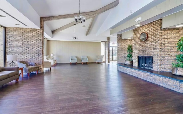 living room featuring vaulted ceiling with beams, a brick fireplace, dark hardwood / wood-style floors, brick wall, and a notable chandelier