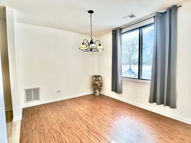 spare room with wood-type flooring and a chandelier