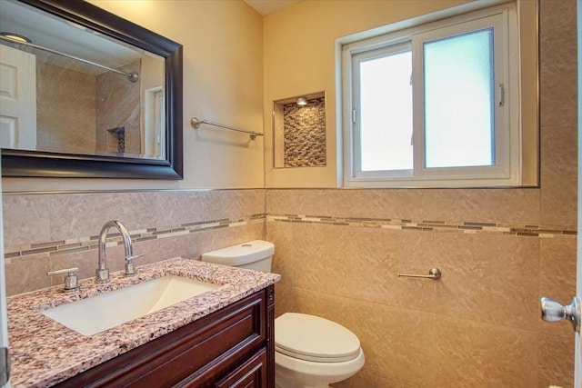 bathroom with tile walls, walk in shower, vanity, and toilet