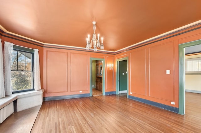 spare room with crown molding, wood-type flooring, radiator, and an inviting chandelier