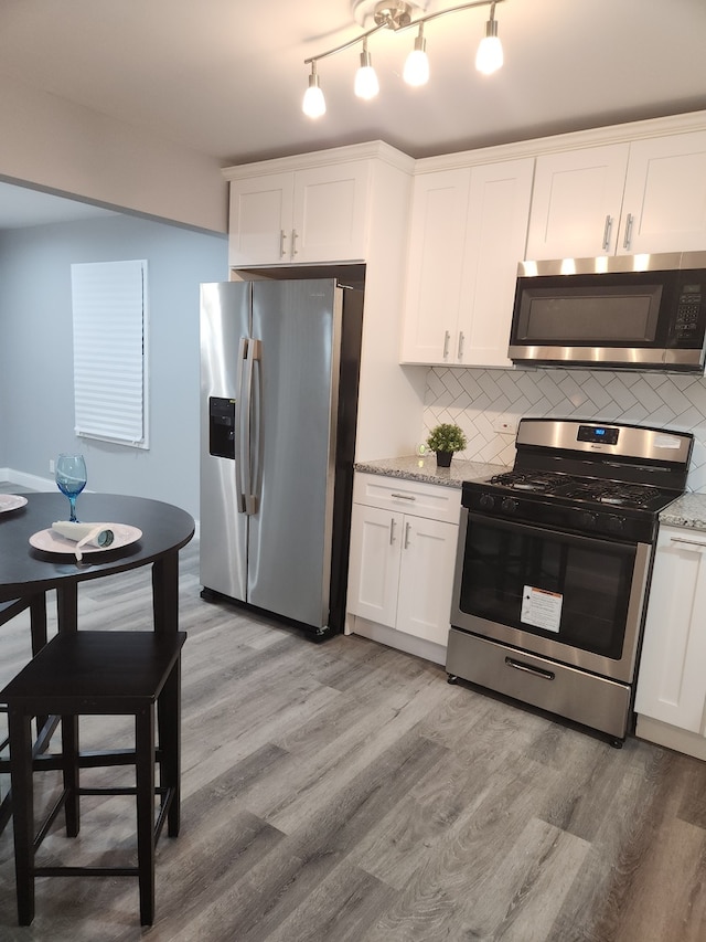 kitchen featuring white cabinets, appliances with stainless steel finishes, light stone countertops, and backsplash