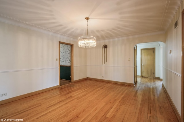 empty room with ornamental molding, hardwood / wood-style floors, and an inviting chandelier