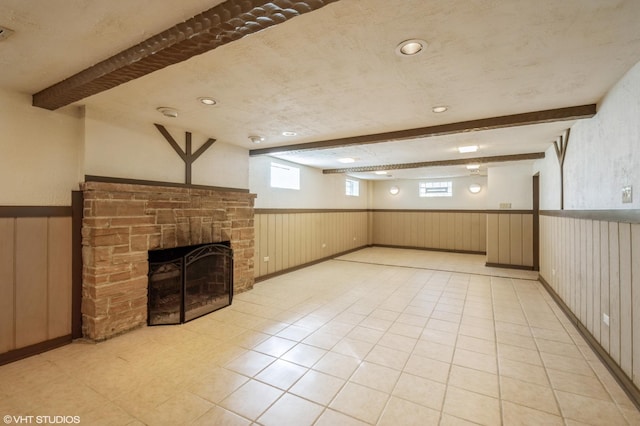 basement featuring light tile patterned flooring, wood walls, a textured ceiling, and a stone fireplace