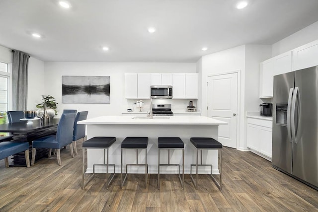 kitchen with appliances with stainless steel finishes, dark wood-type flooring, white cabinetry, and a center island with sink