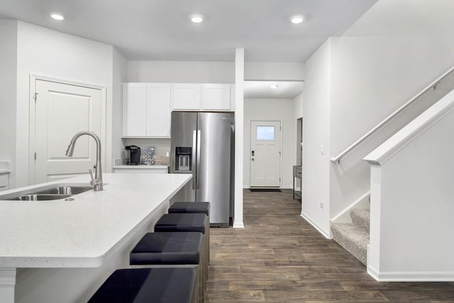 kitchen featuring dark hardwood / wood-style floors, stainless steel fridge, white cabinetry, a kitchen breakfast bar, and sink