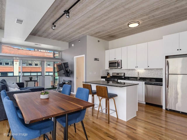 kitchen featuring stainless steel appliances, track lighting, a kitchen bar, and white cabinetry